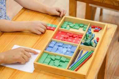 Montessori matematik aracı ile etkileşim halinde olan bir çocuğun yakın plan görüntüsü, elle kullanılan materyallerle matematiksel kavramları öğrenmeye odaklanıyor