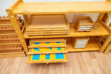 Montessori öğrenimi için düzenli, geometrik şekilli bulmacalı açık çekmeceler de dahil olmak üzere birden fazla eğitim malzemesi içeren ahşap bir raf.