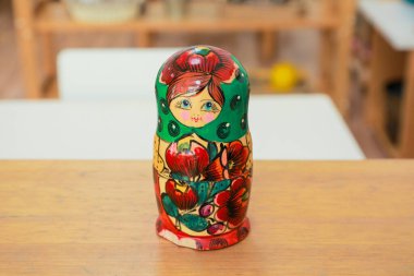 A single vibrant, hand-painted Russian nesting doll with floral motifs displayed on a wooden table indoors, featuring traditional folk art design clipart