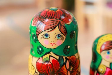 Close-up of a colorful hand-painted Russian nesting doll with a green headscarf and red floral pattern, placed indoors on a wooden surface clipart