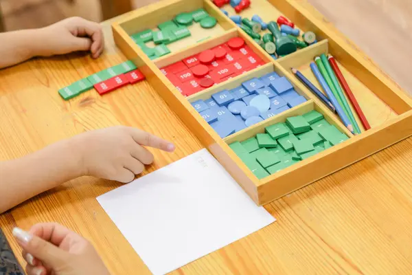 Tahta masa üzerinde eğitim blokları ve materyallerle Montessori matematik araçlarını pratik öğrenme için kullanan bir çocuk