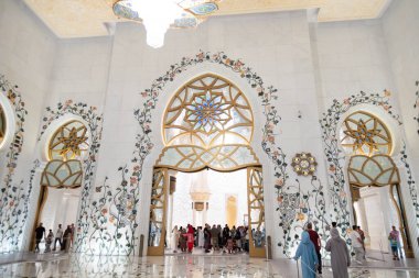 Abu Dabi, BAE - 23 Nisan 2024: Ziyaretçiler Şeyh Zayed Camii 'nin iç kısımlarını keşfettiler, altın, süslü mimaride çiçeklerle süslenmiş kemerler ve boyalı cam aksanlar kullandılar.