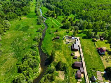 Kırsal evlerin ve geniş yeşil alanların yanından geçen bir nehrin havadan bakış açısı, sakin kırsal manzarayı gözler önüne seriyor.
