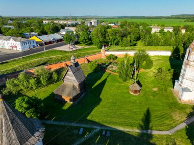 Rusya 'nın Yuryev Polsky şehrine tepeden bakan yeşil bir avlu içinde kırsal ahşap bir kilise ve antik koruyucu duvarları görüntülüyor.