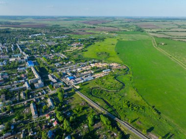 Rusya 'nın Yuryev Polsky kentinde açık mavi gökyüzünün altında geniş yeşil tarla sahalarının yanında şehir gelişimini gösteren bir hava manzarası var.