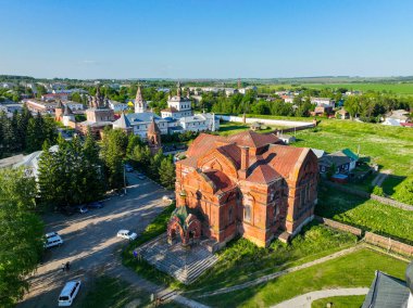 Havadan bakıldığında, Rusya 'nın Yuryev Polsky kentindeki yerleşim yerleri ve ötesinde yeşil alanlar bulunan çarpıcı bir kırmızı tuğla kilise görülüyor.