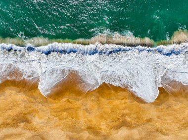 Kıyı dalgaları kıvrılıyor ve kumlu bir plaja dökülüyor görünür bir sörf köpüğüyle