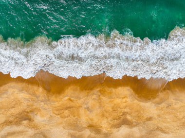 Kıyı dalgaları kıvrılıyor ve kumlu bir plaja dökülüyor görünür bir sörf köpüğüyle