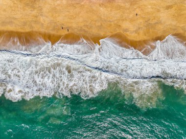 Kıyı dalgaları kıvrılıyor ve kumlu bir plaja dökülüyor görünür bir sörf köpüğüyle