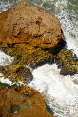 Atlantik Okyanusu dalgaları engebeli sarı ve turuncu kayalara çarpar.