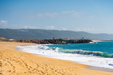 Kumda ayak izleri kayalık bir dalgakıranın yanında çizgili bir deniz feneri ile.