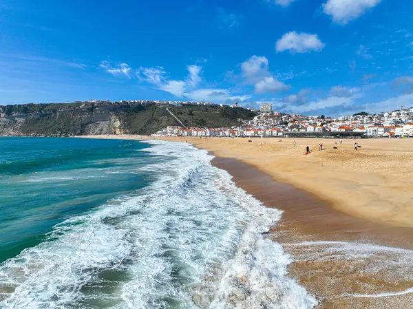 Mavi okyanus dalgası, parlak gün ışığında altın kumun yanında kırılıyor.