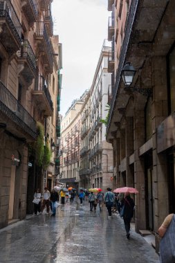 Barselona, İspanya - 12 Mayıs 2023: Dar tarihi bir sokakta hafif yağmurda şemsiye altında yürüyen insanlar