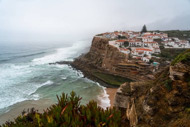 Büyüleyici bir köy, Azenhas do Mar, Atlantik Okyanusu 'nun yukarısındaki sarp kayalıklara tünemiş, aşağı dalgalar çarpıyor ve ön planda yemyeşil bitkiler yeşeriyor.