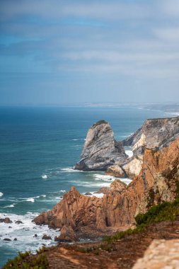 Dramatik çok renkli katmanlı uçurumlar ve yükselen kaya oluşumları kısmen bulutlu bir gökyüzünün altında uçsuz bucaksız mavi Atlantik Okyanusu 'na gururla karşı dururlar.