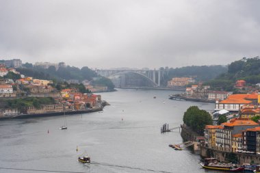 Porto, Portekiz - 12 Mayıs 2024: Douro Nehri 'nin Porto boyunca kıvrılan geniş bir manzarası, nehri kaplayan birden fazla köprü ve bulutlu bir gökyüzü altında yer alan renkli şehir binalarını gösteriyor.