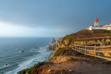 Cabo da Roca deniz feneri, engebeli kıyı şeridi ve okyanus manzaralı altın saat ışığı altında parlıyordu.