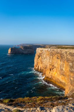 Geniş, dikey bir çekim, Cabo da Roca 'nın altın-kahverengi uçurumlarının büyük ölçeklerini yakalıyor parlak, berrak bir gökyüzünün altında derin mavi Atlantik Okyanusu' na dalıyor.