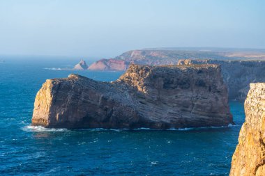 Belirgin, engebeli bir deniz yığını Atlantik Okyanusu 'nun canlı mavi sularında, Cabo da Roca yakınlarında berrak bir gökyüzünün altında görünen uzak kayalıklarda duruyor.