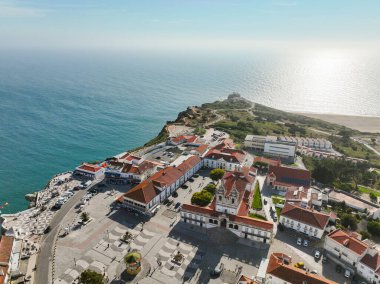 Nazare 'nin tepedeki kilisesinin ve Praia da Nazare ve okyanusa bakan plazanın insansız hava aracı görüntüsü.