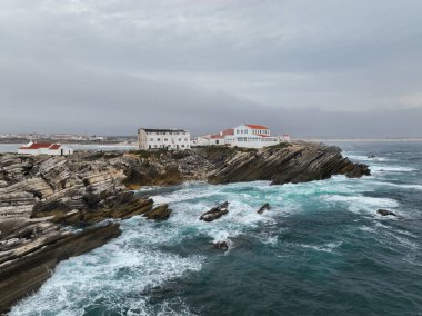 Engebeli kayalıkların kıyısındaki dalgalı binaların alçak drone görüntüsü