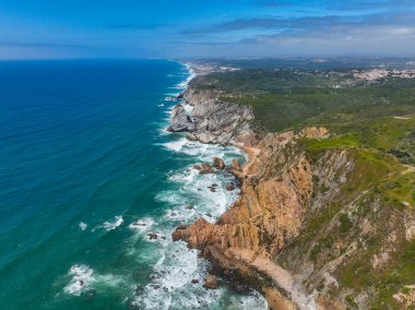 Canlı turkuaz okyanus sarp kayalıklara ve kaya oluşumlarına çarpıyor.