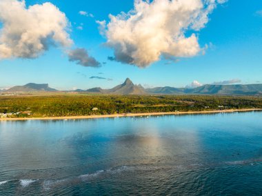 Flic en Flac plajının havadan görünüşü evler ve ormanlarla dolu, arkasında dramatik dağlar var.