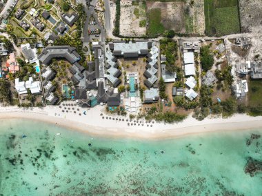 Şemsiyeli, bitişik binalı ve tarım arazili sahil manzaralı tepeden tırnağa bir tatil köyü.