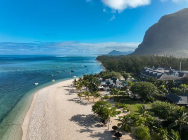 Şemsiyeler ve tropikal tatil beldeleriyle dolu kumlu kumsalın insansız hava aracı görüntüsü.