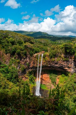 Mauritius 'taki Chamarel Şelalesi' nin panoramik görüntüsü açık mavi bir gökyüzünün altındaki orman vadisine dökülüyor.