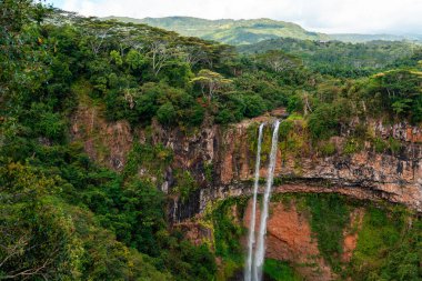 Mauritius 'taki Chamarel Şelalesi' nin panoramik görüntüsü açık mavi bir gökyüzünün altındaki orman vadisine dökülüyor.