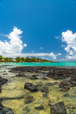 Şeffaf göl suyu, tropikal kıyı şeridine demirlemiş teknelerle karanlık kayaların üzerinden akıyor.