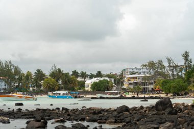 Le Morne, Mauritius - 12 Mayıs 2024: Sahil boyunca sığ sularda demirlemiş teknelerle binaların ve palmiye ağaçlarının yakın görüntüsü