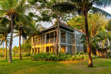 Le Morne, Mauritius - 12 Mayıs 2024: Kapalı panjurları ve sıcak günbatımı parıltısıyla aydınlatılmış palmiye ağaçları olan büyüleyici iki katlı bir tatil köyü.