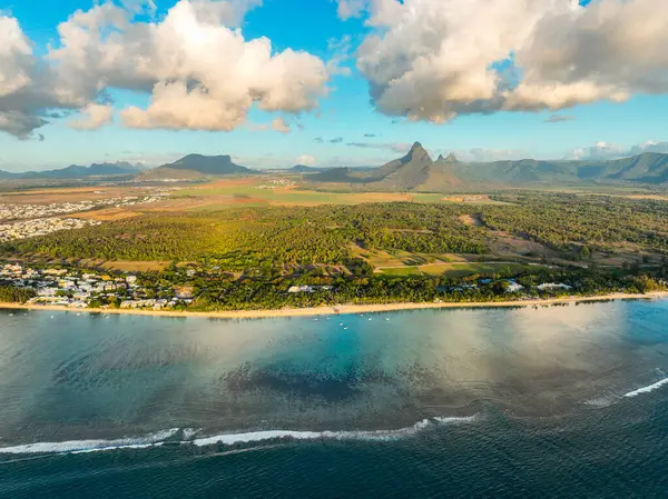 Flic en Flac plajının havadan görünüşü evler ve ormanlarla dolu, arkasında dramatik dağlar var.