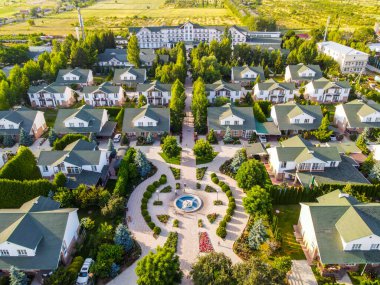 Balykchy, Kırgızistan - 12 Mayıs 2023: Sıralı konut evleri, merkezi bir çeşme ve yemyeşil peyzaj ve ağaçlarla dolu bir tatil köyünün havadan görünüşü