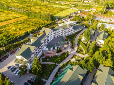 Balykchy, Kırgızistan - 12 Mayıs 2023: Yeşil çatıları, yemyeşil bahçeleri, kaldırımları ve bir otoparkı olan büyük bir otel binasının havadan görünüşü