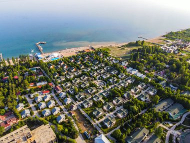 Sayısız kulübesi, kumlu bir plajı ve dingin bir göle uzanan rıhtımı olan bir tesisin geniş hava manzarası.