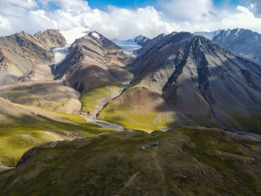 Bir grup aracın dramatik ve engebeli bir dağ manzarasında, küçük bir tepeye park edilmiş, karla kaplı tepeleri olan bir grup aracın insansız hava aracı görüntüsü.