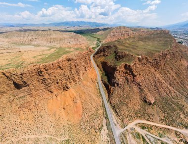Uçsuz bucaksız, kuru, kayalık bir araziyi kesen dolambaçlı bir yol. Uzak bir şehir ve açık bir gökyüzü altında karla kaplı dağlar.