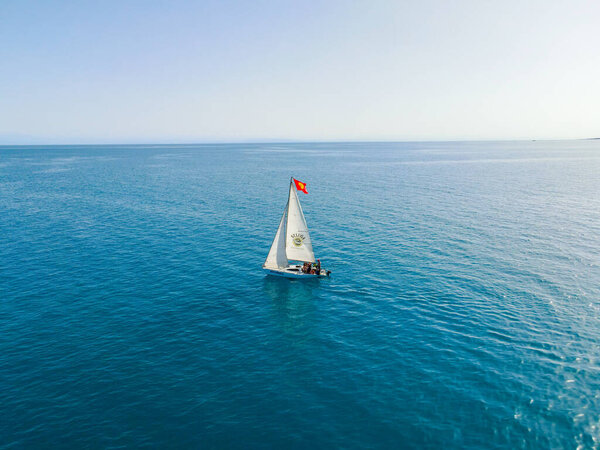 Балыкчи, Кыргызстан - 12 мая 2023 года: Снимок беспилотника, показывающий парусник с красным и желтым флагом, плывущий по голубому озеру под ясным небом