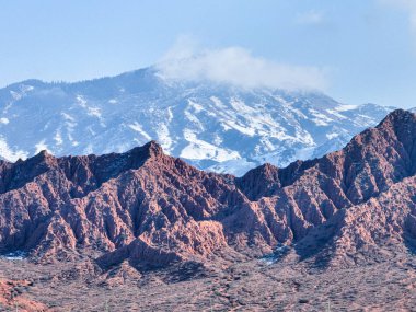 Mars Kanyonu 'nun engebeli kırmızı oluşumları, açık bir gökyüzünün altında sisli kar kaplı bir dağla ön planda duruyor.