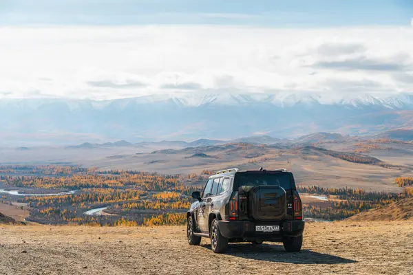 Aktash, Altai Cumhuriyeti - 12 Ekim 2023: Siyah bir Jetour T2 SUV 'nin arka tarafı manzaralı bir sonbahar dağ vadisine bakan yüksek bir toprak yolda park halinde görüldü.