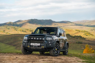 Aktash, Altai Cumhuriyeti - 12 Ekim 2023: Siyah bir Jetour T2 SUV, rengarenk sonbahar yeşillikleriyle kaplı güzel, yuvarlanan dağlarla dolu bir tepenin üzerine park edilmiştir.