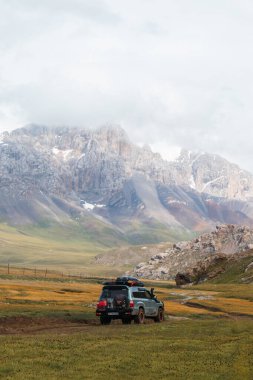 Naryn, Kırgızistan - 12 Ekim 2024: Toyota Land Cruiser bulutlu bir gökyüzünün altında engin, yeşil ve altın bir vadide bulunur.