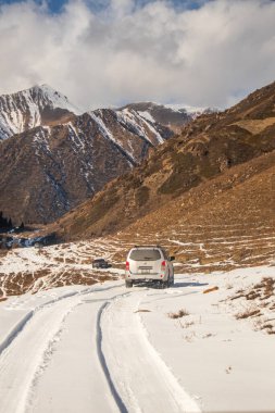 Naryn, Kırgızistan - 12 Ekim 2024: İki off-road aracı, arka planda karlı bir dağ sırası olan engin bir vadide karlı bir dağ yolunda ilerliyor