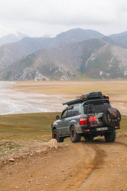 Naryn, Kırgızistan - 12 Ekim 2024: Toyota Land Cruiser uçsuz bucaksız bir vadide, kurumuş bir nehir yatağı ve engebeli dağlarla toprak bir yolda ilerliyor.
