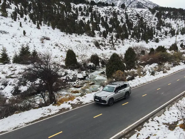Bishkek, Kyrgyzstan - December 12, 2024: The new Lexus LX luxury SUV is seen driving on a paved road alongside a river in a snowy mountain landscape