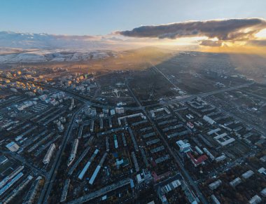 Kırgızistan, Bişkek 'in çarpıcı yüksek irtifalı hava manzarası, gün batımında bulutların arasından yükselen dramatik güneş ışınlarını yakalıyor, arka planda karla kaplı dağlar var.