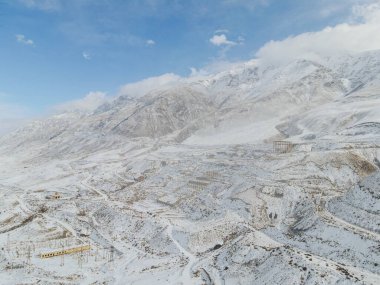 Kırgızistan dağlarındaki eski bir Sovyet maden hayalet kasabası olan Enilchek 'in dağınık harabelerini ve altyapısını gösteren engin, karla kaplı bir manzara.